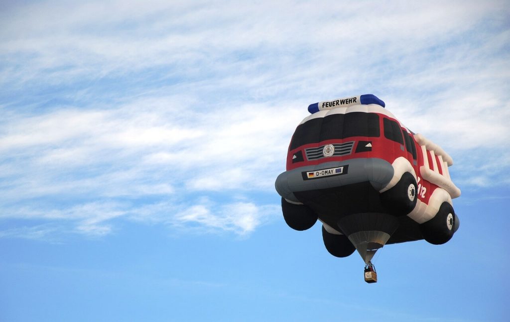 A playful hot air balloon resembling a fire truck soars through the sky.